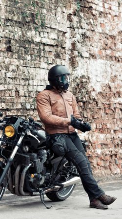 Man,A,Motorcyclist,Standing,With,Helmet,Near,Her,Bike,,Brick